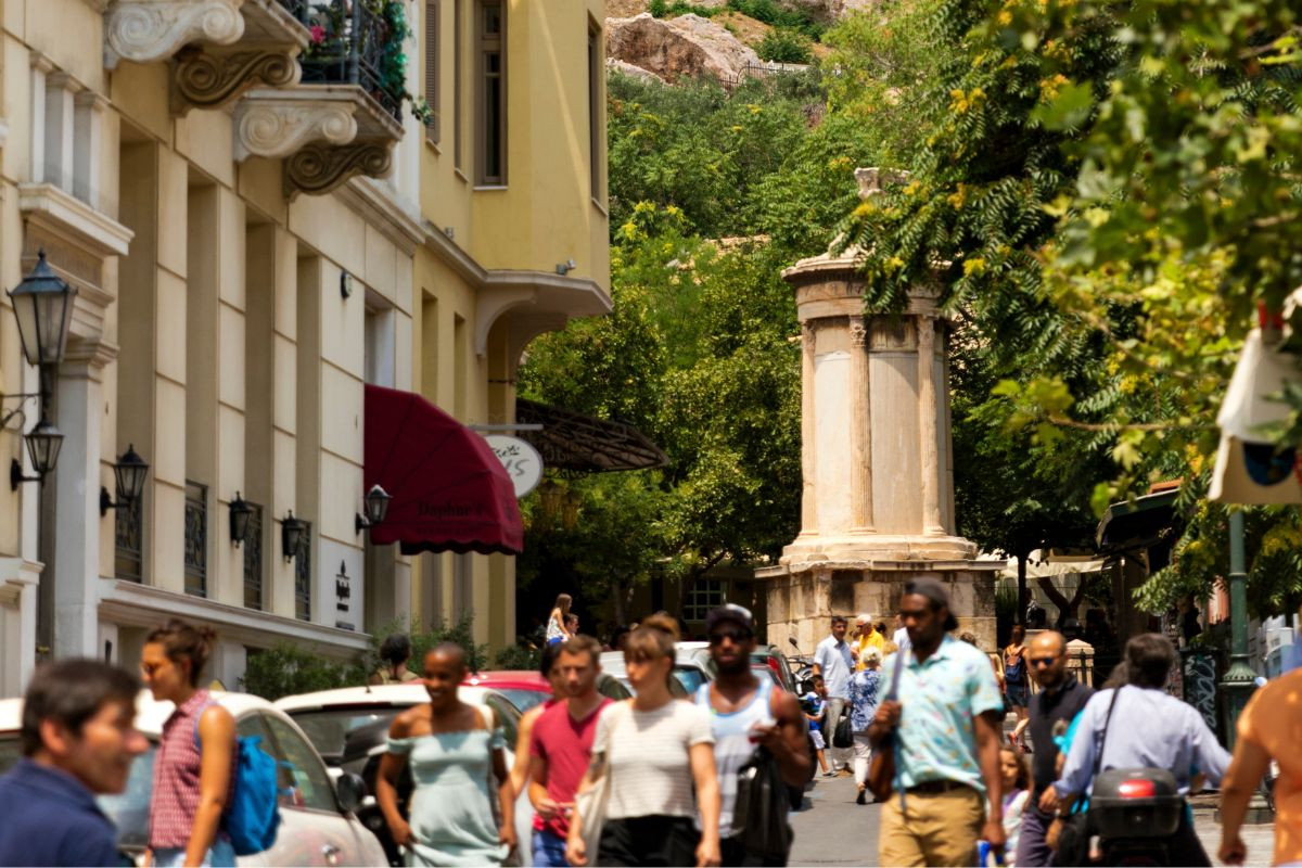 A bustling street scene with pedestrians and a glimpse of an ancient column in the background.